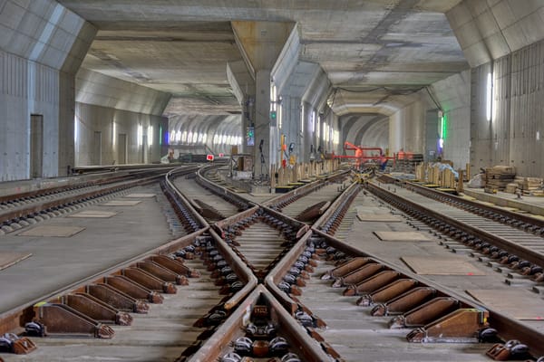 Eisenbahnschienen kreuzen sich in einem hell erleuchteten Betontunnel mit gewölbten Decken und Bauarbeiten.