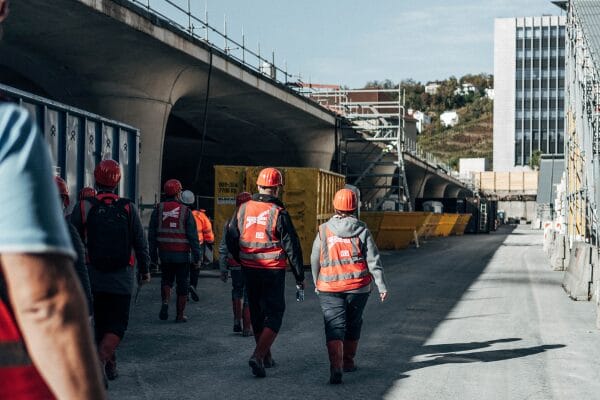 Bauarbeiter mit roten Helmen gehen mit Gerüsten die Baustraße am Neuen Hauptbahnhof entlang.