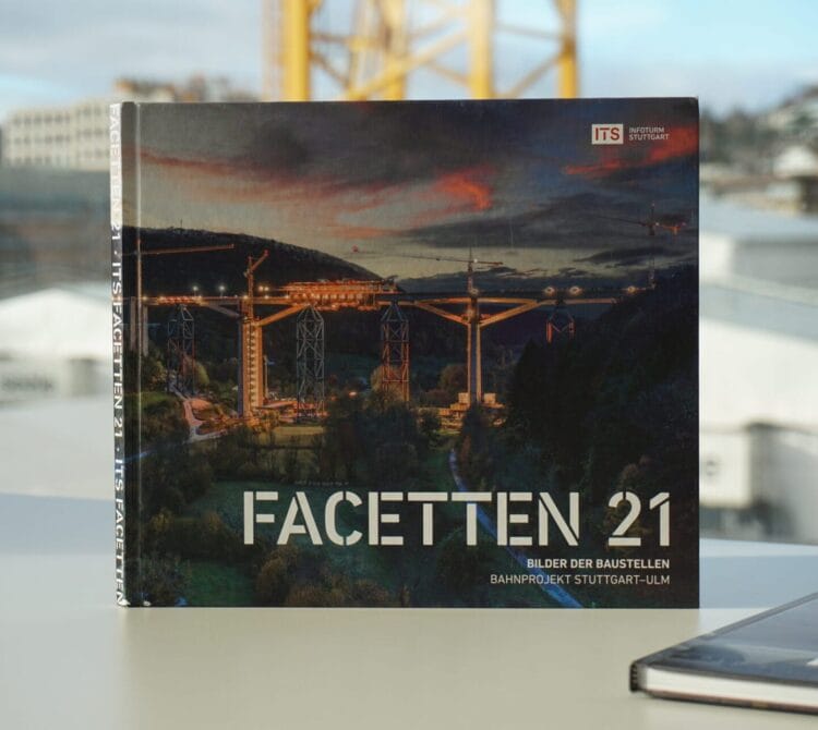 Buch "Facetten 21" auf einem Tisch; Umschlag zeigt nächtliche Bauarbeiten mit Brücke, Kränen, Stadt.