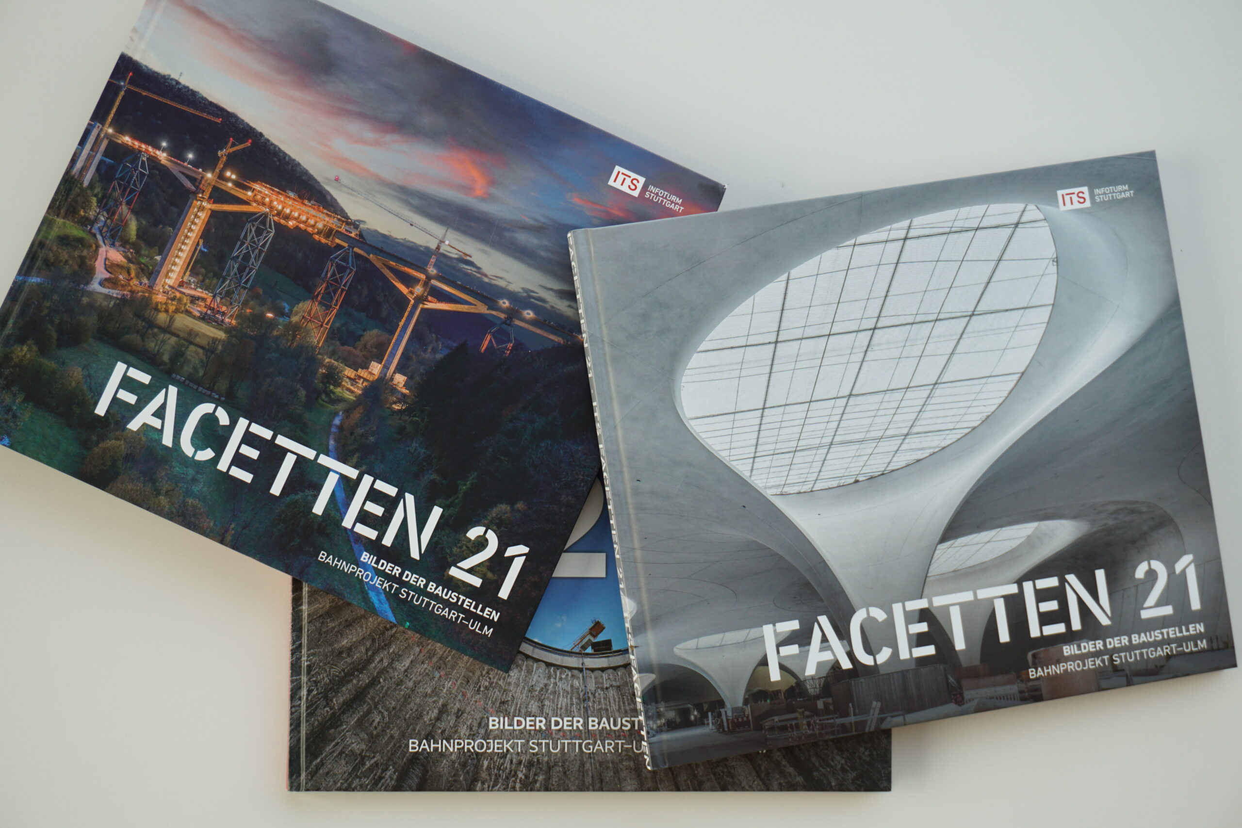 Drei "FACETTEN 21"-Bücher mit Bau- und Architektureinbänden, überlappend auf weißer Fläche.